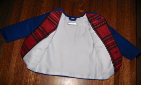 Front view of blue coat, opened to reveal red plaid facing, white satin lining, and blue wool hanging loop